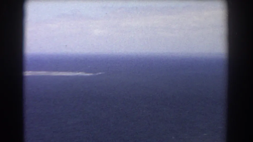 1967 Perth, Australia aerial 8mm frame looking across open ocean toward a thin pale surf or sand line beneath a bright hazy sky.