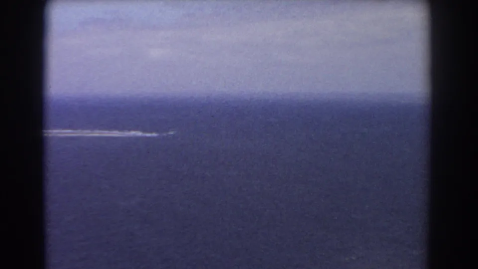 1967 Perth, Australia aerial frame showing broad blue ocean, a distant white shoreline or surf break, and muted 8mm color under haze.