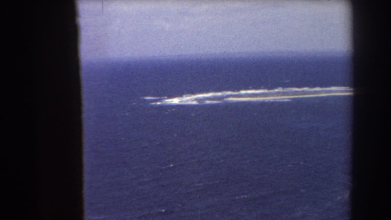 Blue ocean with a long pale feature and white surf seen through dark film borders.
