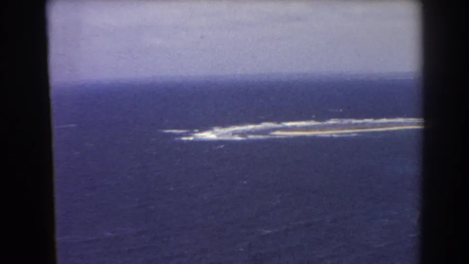 1967 8mm Perth-area aerial view showing a long grey ocean feature with surf lines and a broad cloudy sky band.