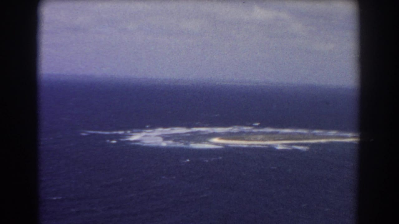 1967 8mm aerial view near Perth, Australia, showing a small low island or reef ringed by surf in open ocean.