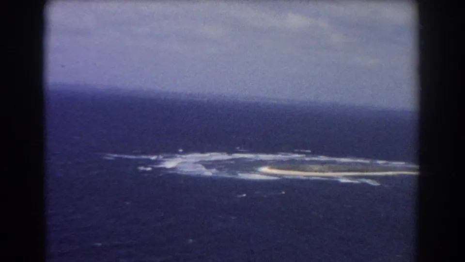 1967 8mm passenger-window view of a low island or reef formation in the ocean near Perth, Australia.