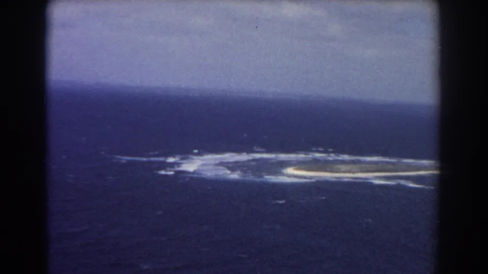 Aerial 8mm frame from 1967 showing a remote ocean island or reef as the aircraft moves past it near Perth, Australia.