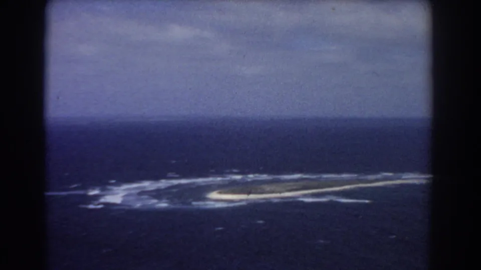 1967 8mm aerial view near Perth, Australia, with a low island or reef set against dark blue ocean and muted sky.
