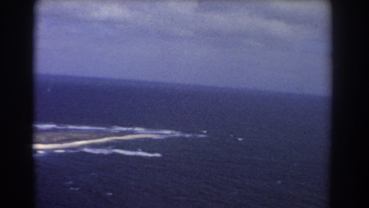 1967 8mm aerial view near Perth, Australia, showing a low island partly framed by surf and deep blue sea.