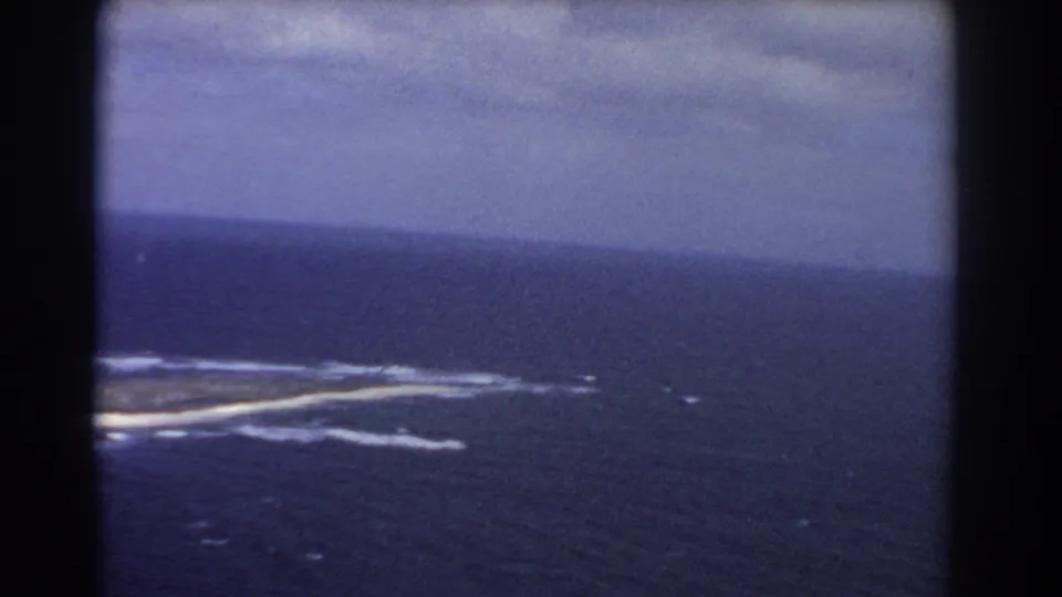 1967 8mm aerial view near Perth, Australia, showing a low island partly framed by surf and deep blue sea.
