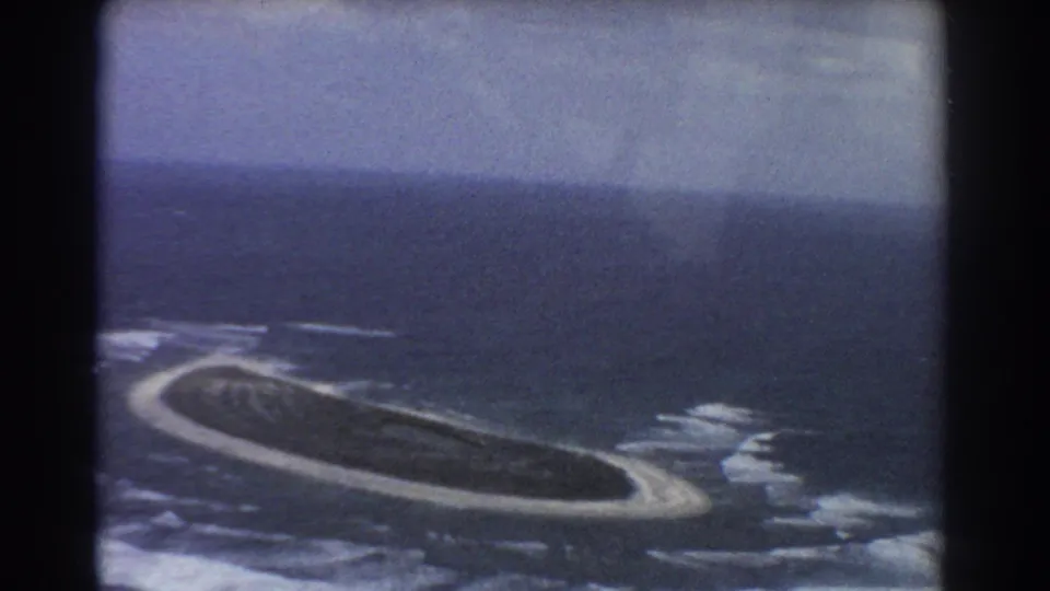 Aerial 8mm frame near Perth showing the same small island, white shoreline, and surrounding blue water.