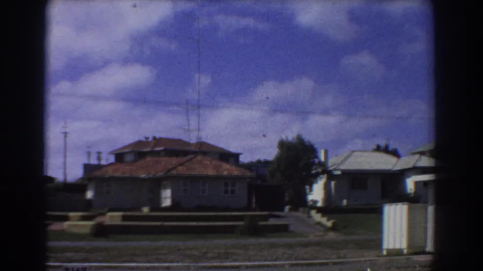 1967 Perth suburban view with low houses, tiled roofs, a driveway or path, roadside edge, utility poles, and partly cloudy sky.