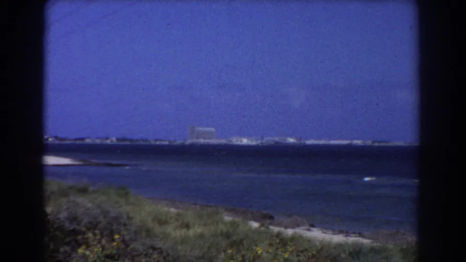 Final 1967 Perth-area 8mm frame holds on the ocean, grassy shoreline, and distant coastal buildings.