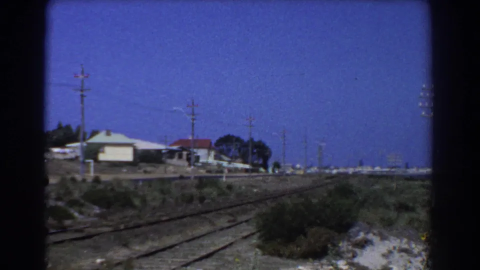 1967 Perth rail-side view with parallel tracks, modest houses, telephone or power poles, and a clear blue sky.
