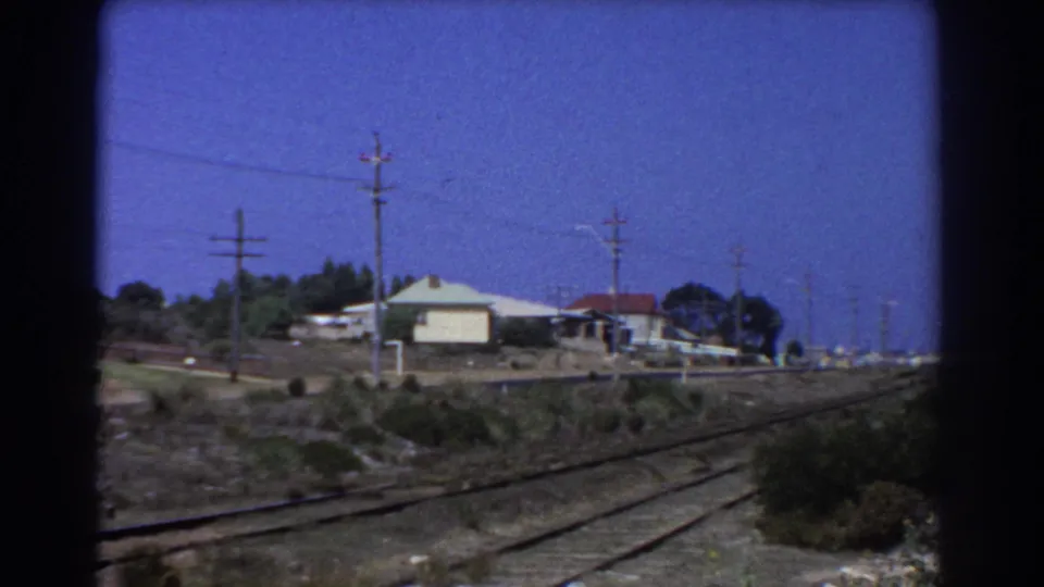 1967 Perth home-movie view showing rail tracks beside low houses, utility poles, and rough open ground.