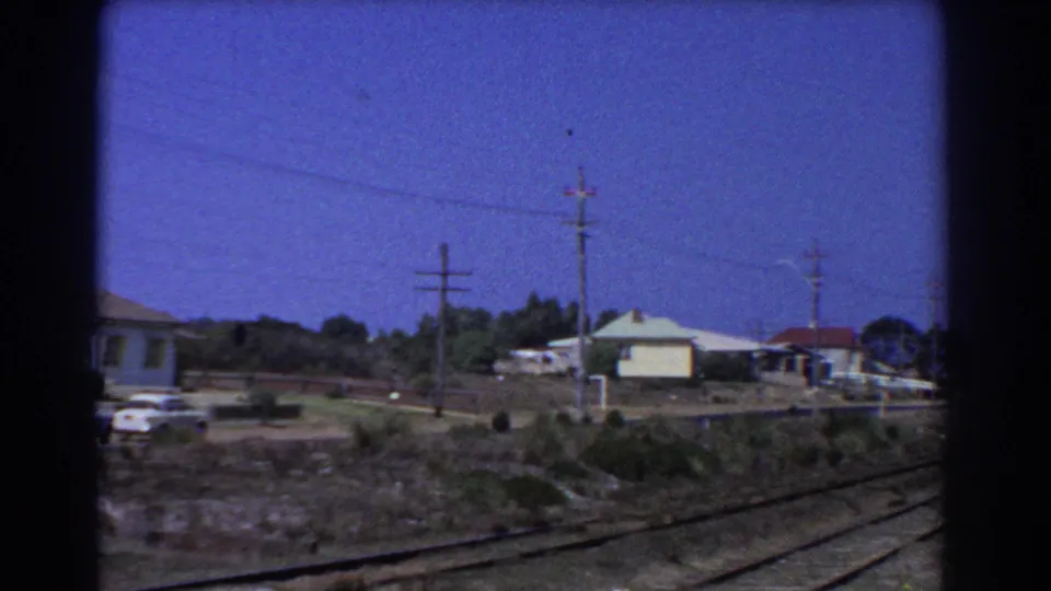 1967 Perth frame with rail tracks in the foreground, low houses, utility poles, overhead wires, and a parked car.