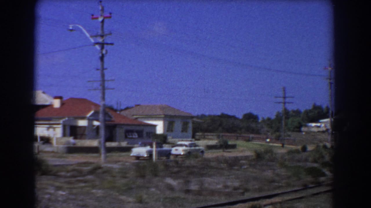 Houses with red roofs, parked cars, power poles, and tracks in the foreground.
