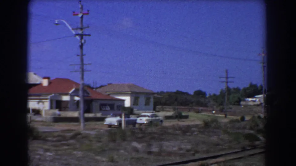 Perth neighborhood houses in 1967 appear beyond rail-side ground, with parked cars, utility poles, overhead lines, and clear sky.
