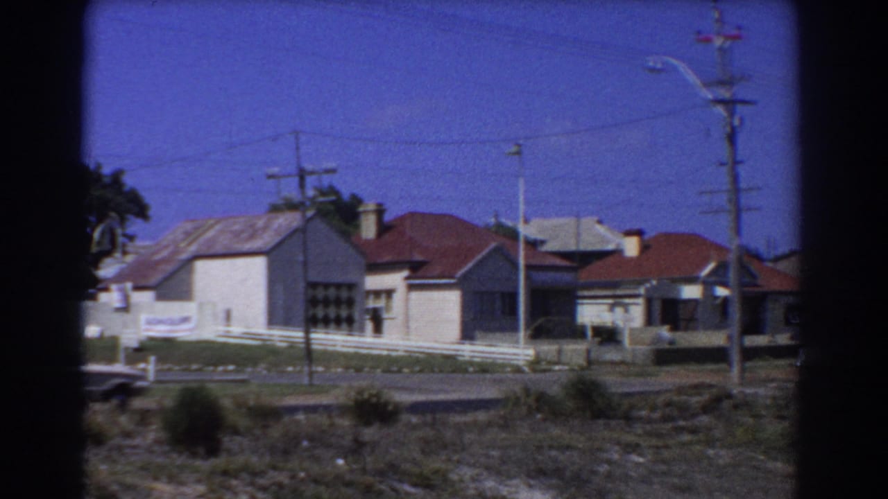 1967 Perth suburban street view with single-story houses, white fencing, utility poles, and dark rounded frame edges.