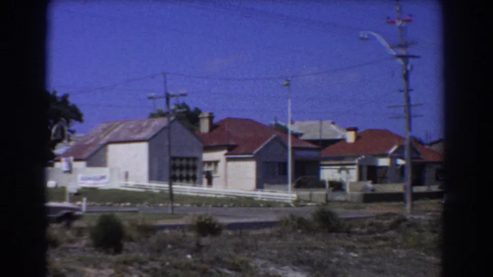 1967 Perth suburban street view with single-story houses, white fencing, utility poles, and dark rounded frame edges.