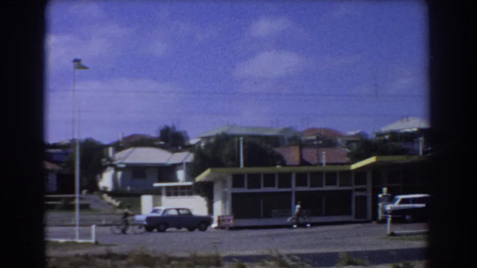 1967 Perth 8mm frame showing a service station from across the street, with a cyclist, a pedestrian and parked cars in view.