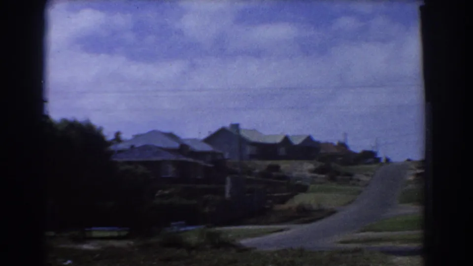 Final frame of the 1967 Perth street view, showing empty roadway, suburban roofs, verges, and handheld 8mm framing.