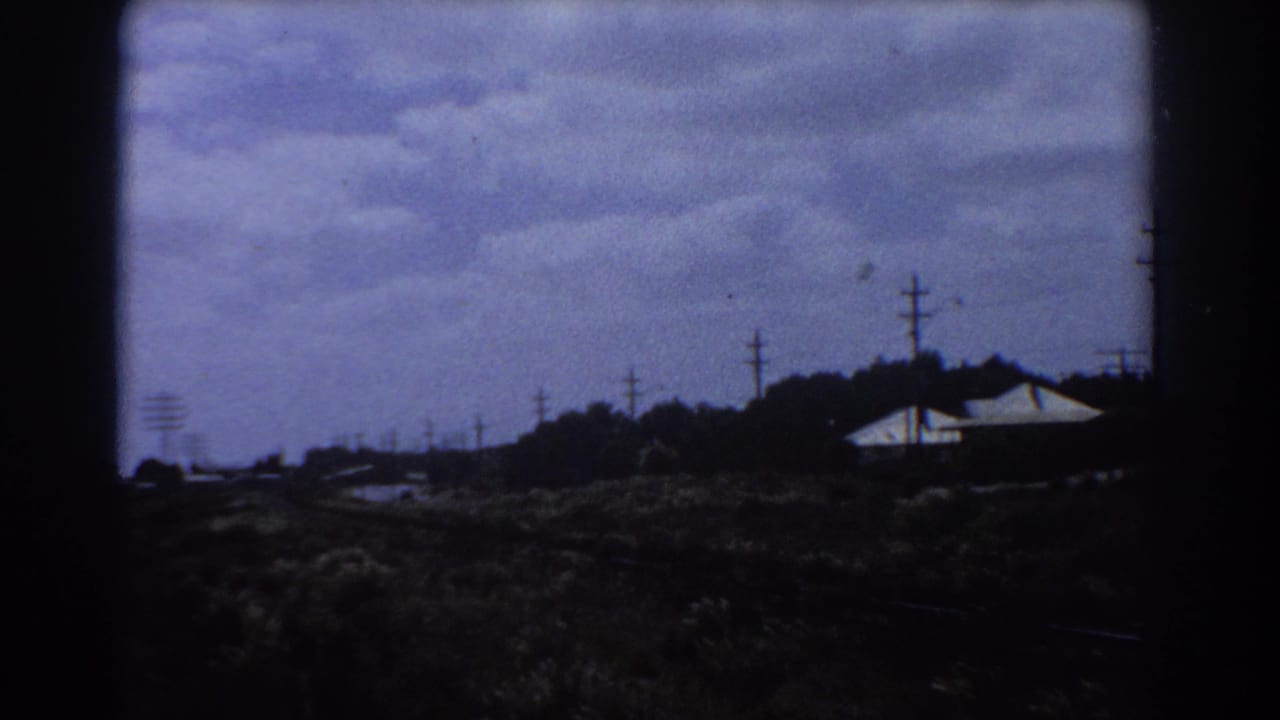 Distant white-roofed buildings beyond dark grassy rail-side ground and utility poles.