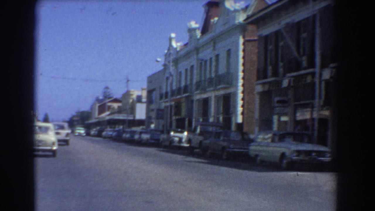 Quiet city street lined with parked cars and older commercial buildings.