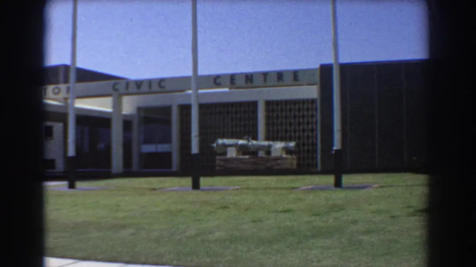 Perth Civic Centre exterior with entrance sign, flagpoles, green lawn, and an outdoor cannon display.
