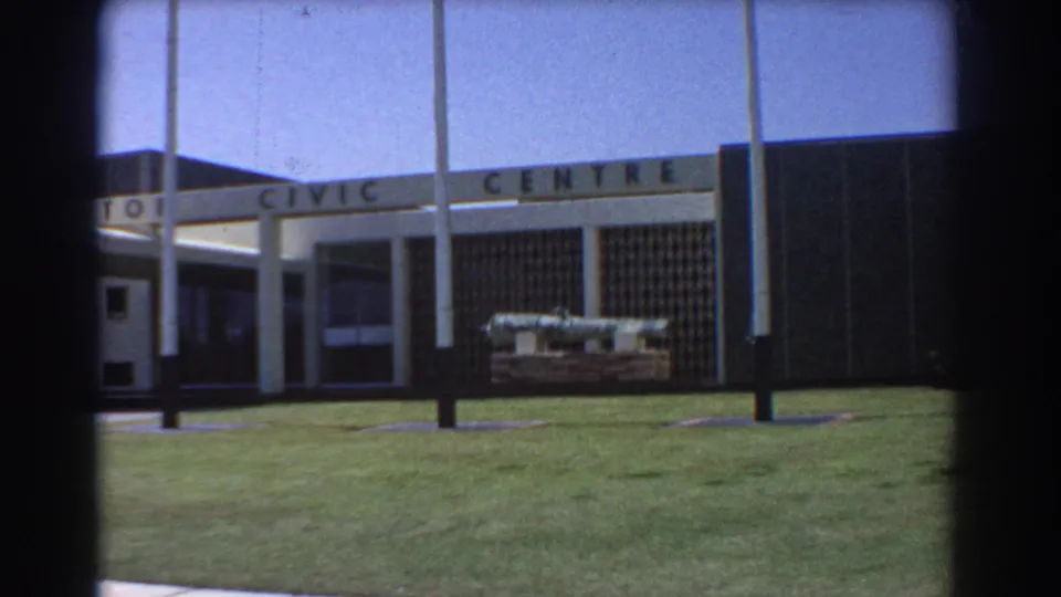 Perth Civic Centre exterior remains in view, with flagpoles crossing the sign and a cannon display on the grass.