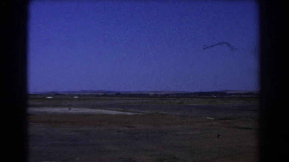 Flat dry fields near Perth appear beneath a broad blue sky, framed by dark 8mm gate edges and visible film grain.