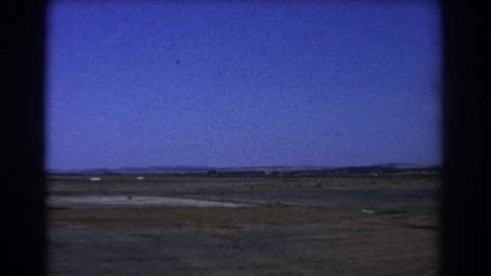 1967 Perth-area home-movie frame showing flat open fields, a distant tree line, and a large blue sky within visible 8mm gate edges.