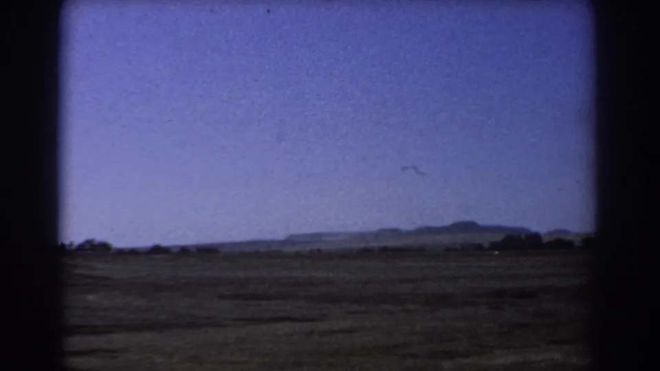 1967 Perth landscape frame with green-brown fields, low hills in the distance, scattered tree shapes, and dark 8mm gate edges.