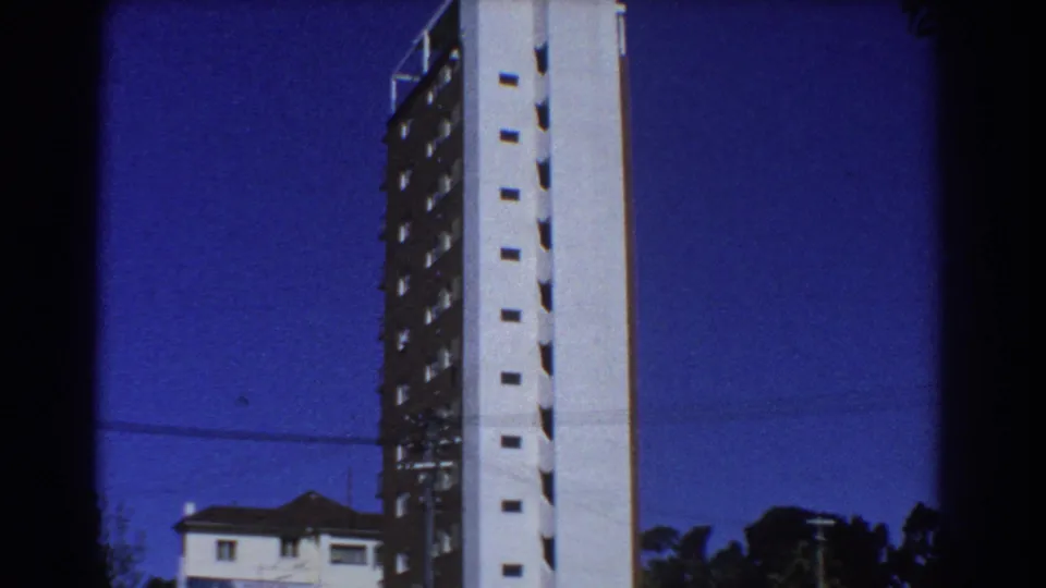 1967 Perth exterior view with a high-rise facade, nearby residential roofline, trees and visible 8mm frame edges.