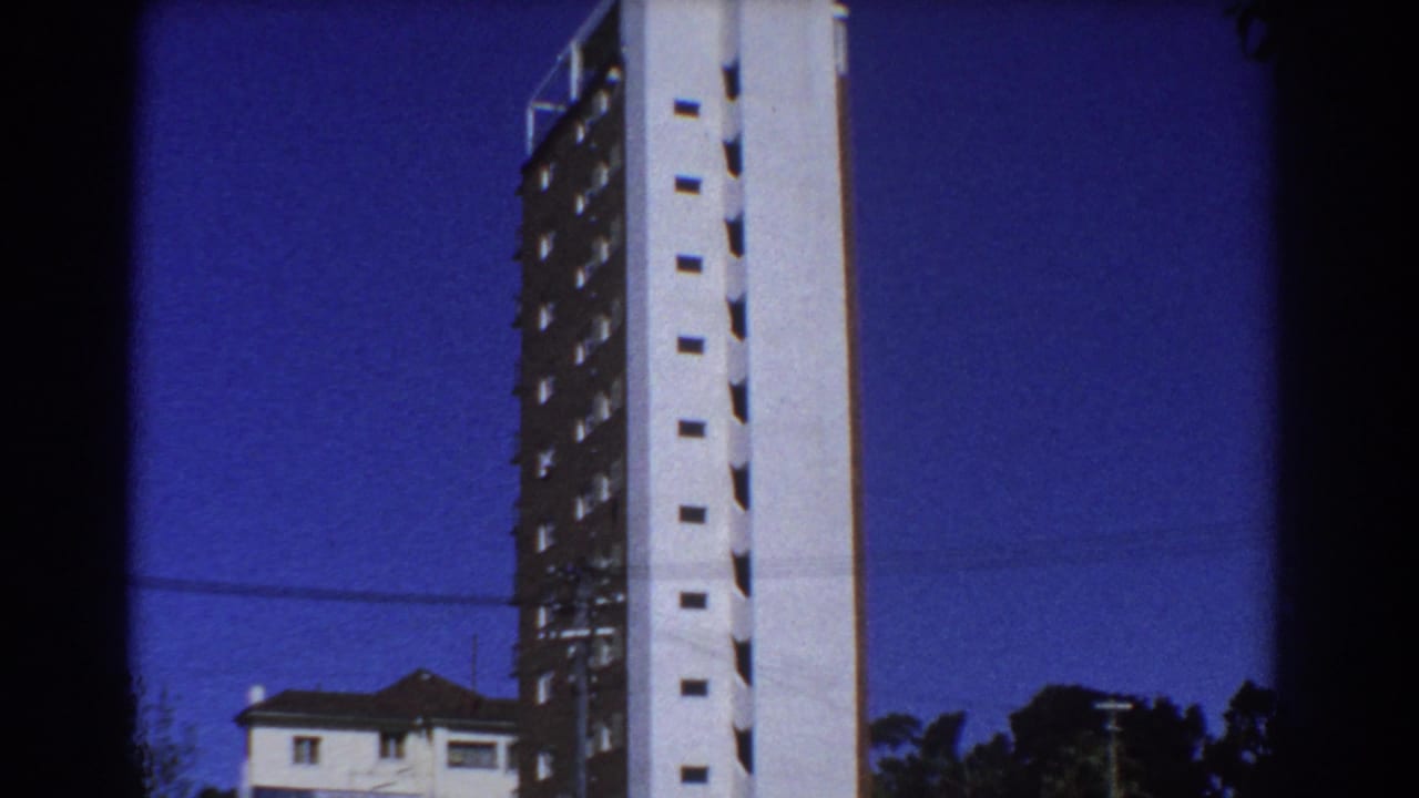 Tall completed building beside rooftops under a blue sky.