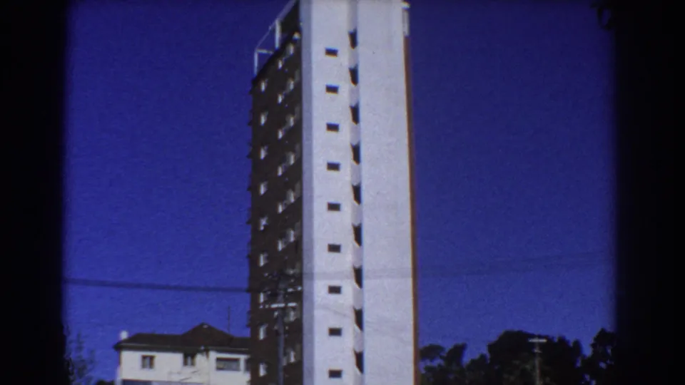 Perth 1967 home-movie frame showing a completed high-rise above nearby residential roofs and trees.