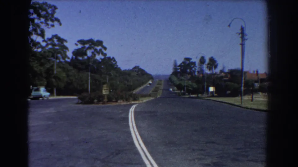 1967 Perth street view looking down an empty curving road lined with trees, streetlights, and residential edges.