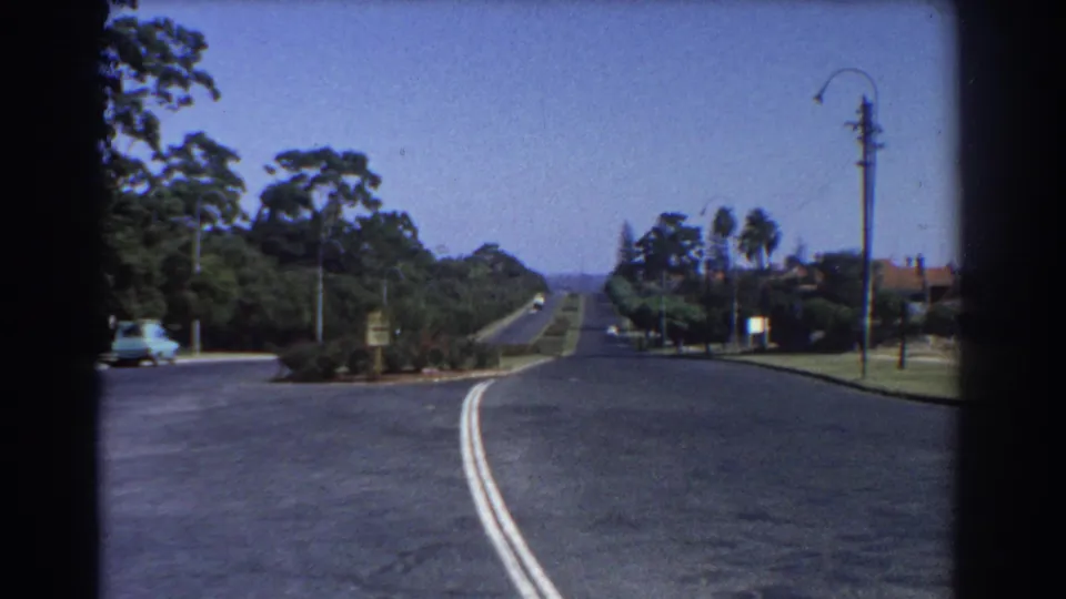 Perth residential road scene from 1967, with a broad empty street, double center lines, trees, streetlights, and houses at the edge.