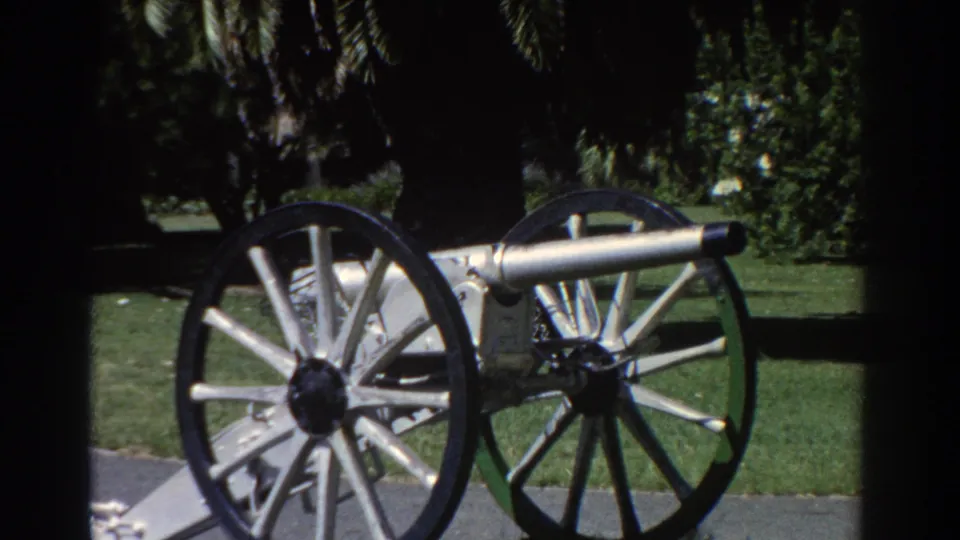 1967 Perth home-movie frame showing a restored silver cannon on spoked wheels in a shaded public park.