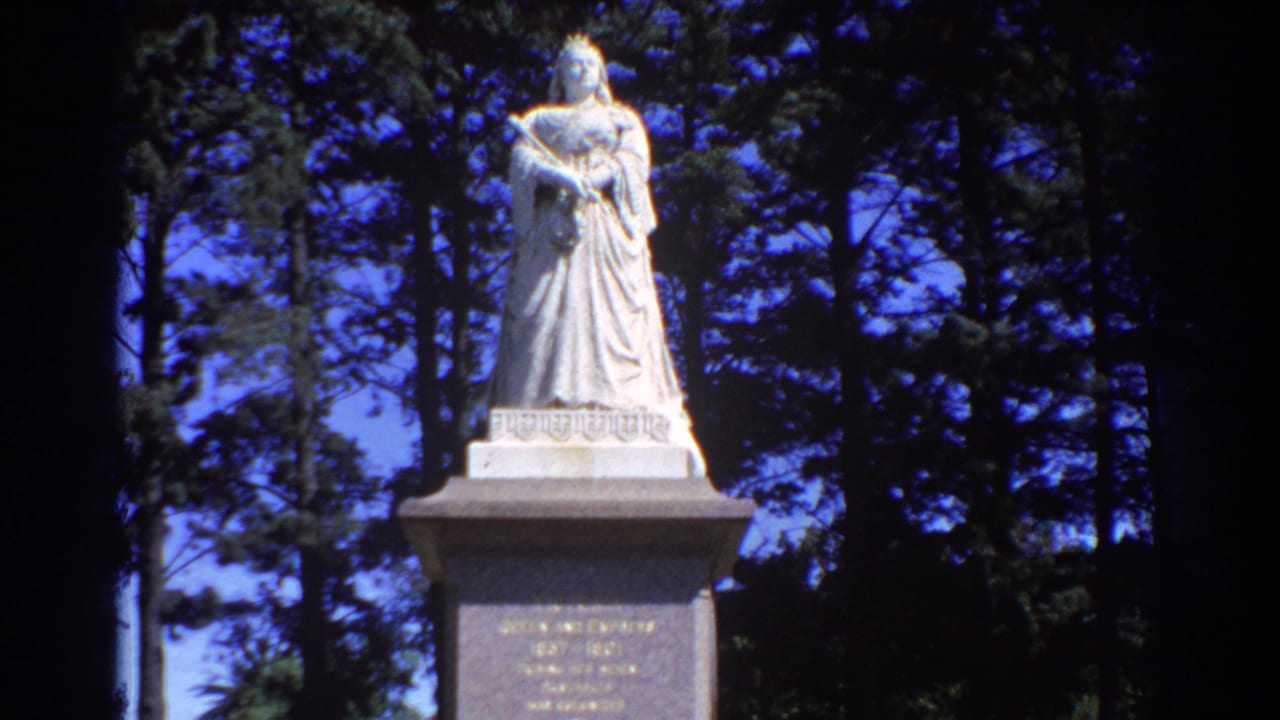 Stone statue of a robed woman on a pedestal among tall trees.