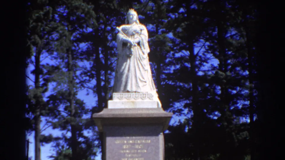 1967 Perth 8mm frame with the statue centered high on its pedestal, backed by dark trees and vivid sky.