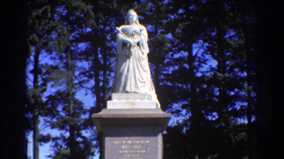 1967 Perth 8mm frame showing the pale robed statue on its plinth, contrasted with deep tree shadows behind it.