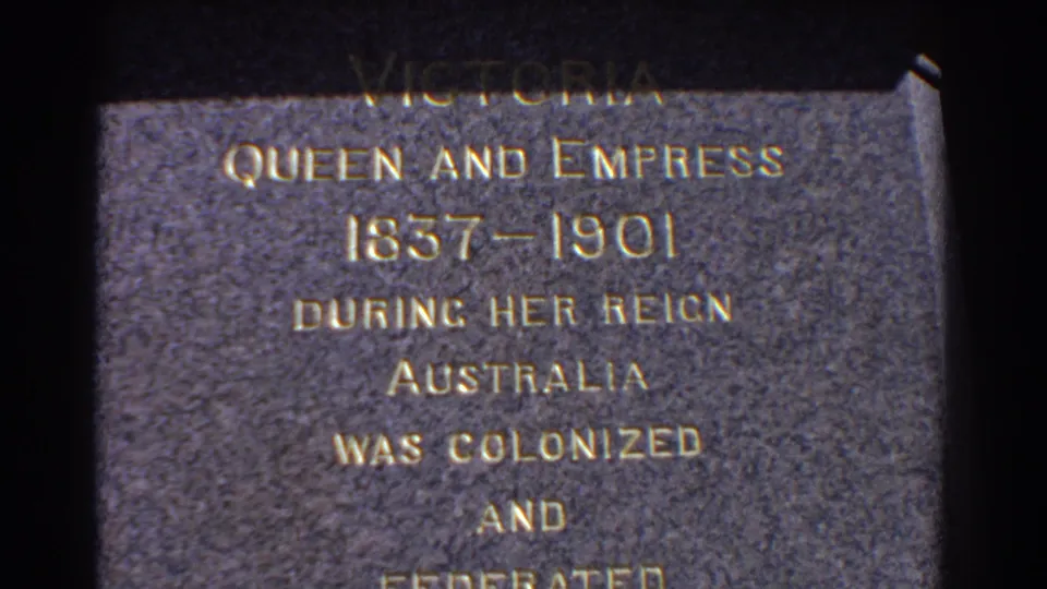 Close 8mm frame of the Perth memorial plaque reading Victoria Queen and Empress, with dates and lines about Australia partly visible.