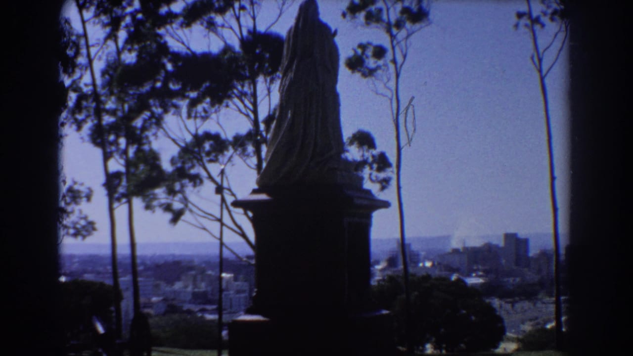 Silhouetted statue on a hillside with trees and distant city buildings below.