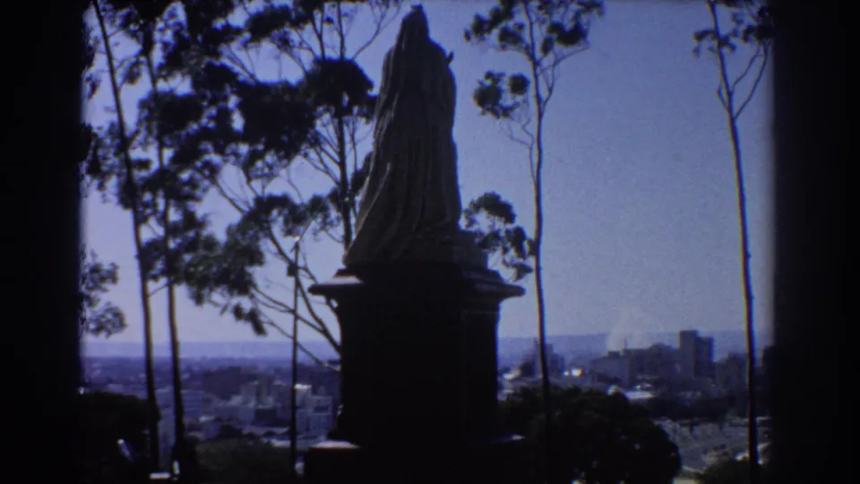 1967 8mm frame showing the hillside statue in silhouette with Perth buildings faintly visible below.