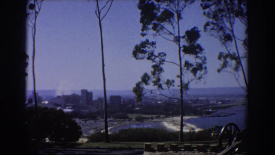 1967 Perth hillside view with trees in the foreground, distant buildings, and water or shoreline at right.