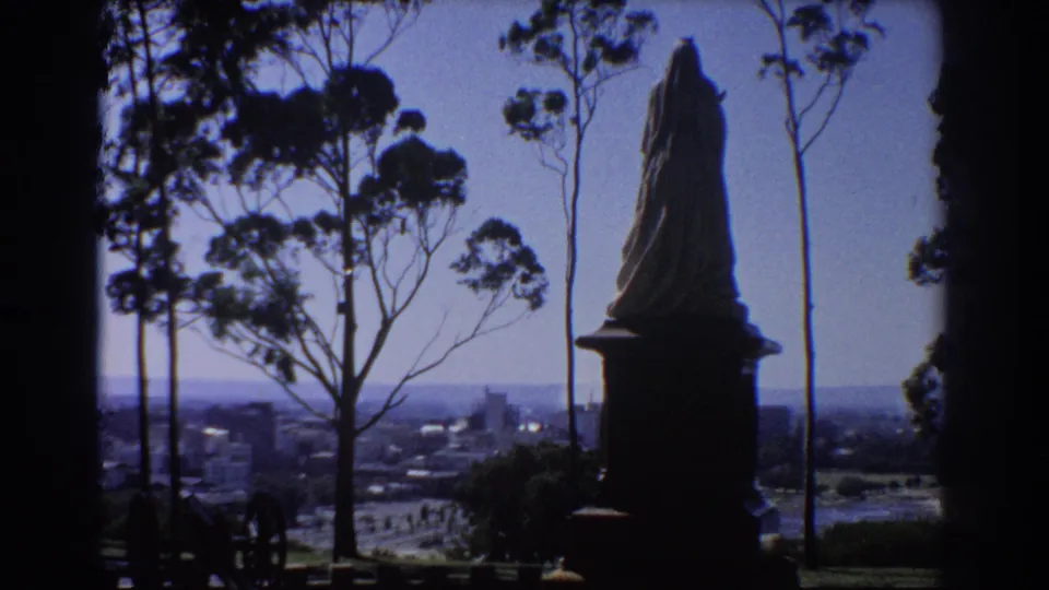 Final 1967 Perth hilltop frame with the statue at right, eucalyptus trees at left, and buildings receding in haze.