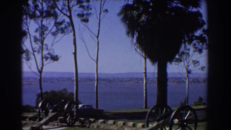 1967 Perth park overlook with windblown trees, cannons, grass, and a calm blue water horizon.