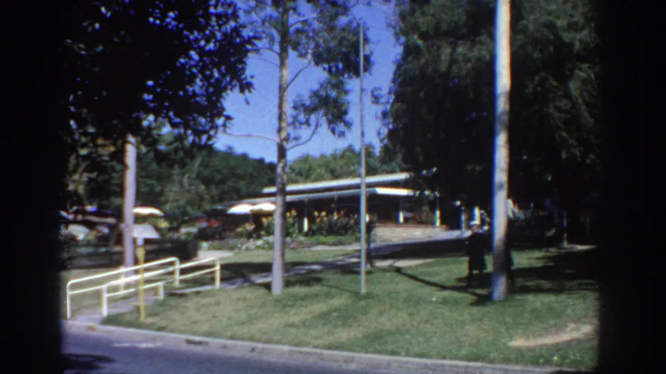 Perth, Australia frame from 1967 with a modernist-looking building, shaded outdoor seating, lawns, railings, and a distant walker.