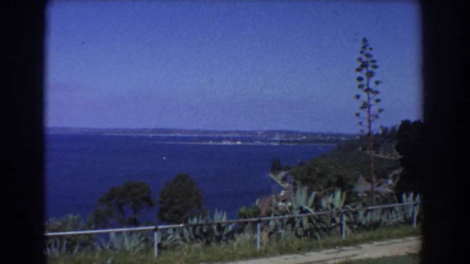 1967 Perth coastal overlook with low fence, shrubs, trees, path, blue sea, and distant shoreline.