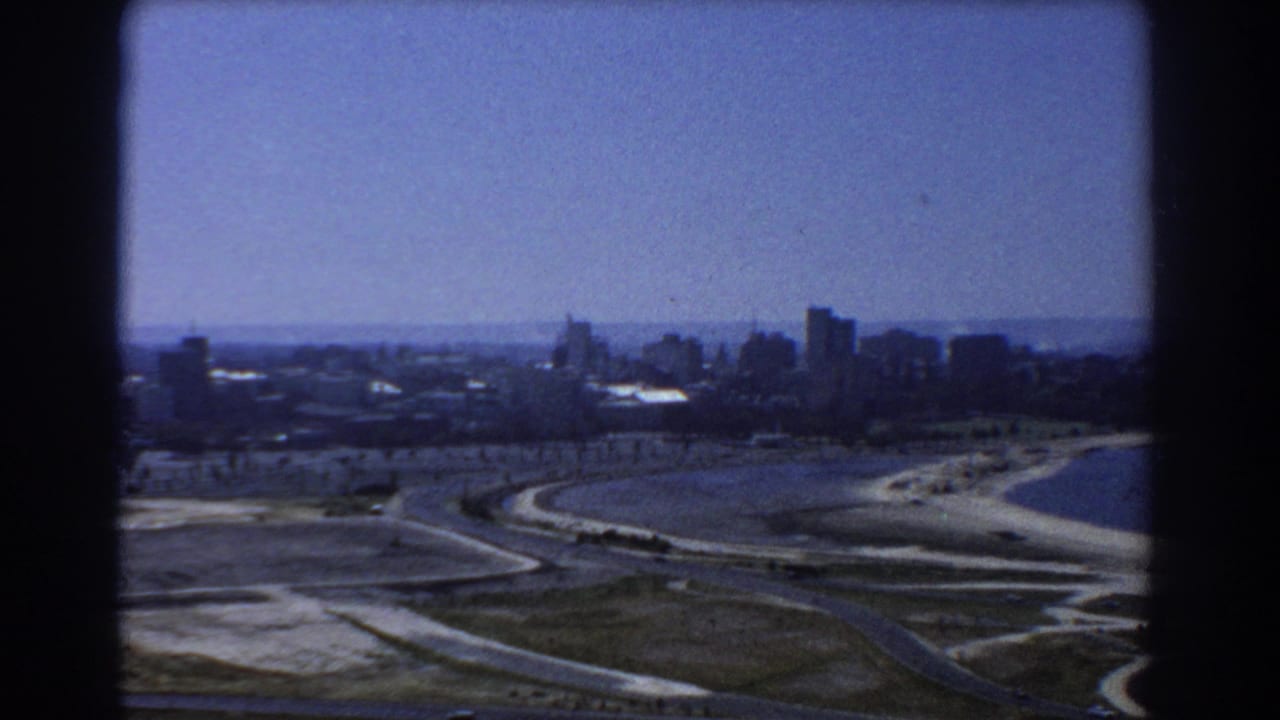 Distant city skyline beyond curving roads and shoreline from a high vantage point.