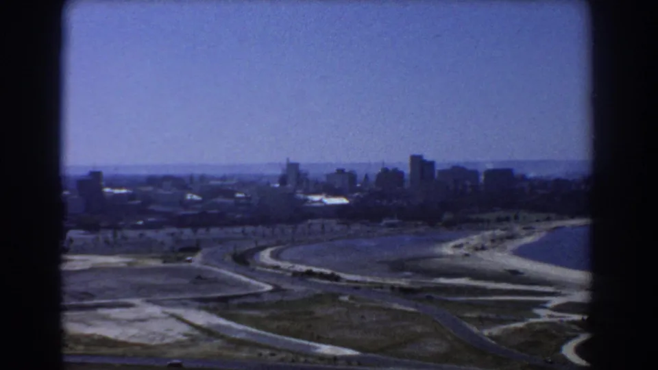 Elevated 1967 Perth coastal view with skyline in the distance, sandy beach at right and winding roads below.