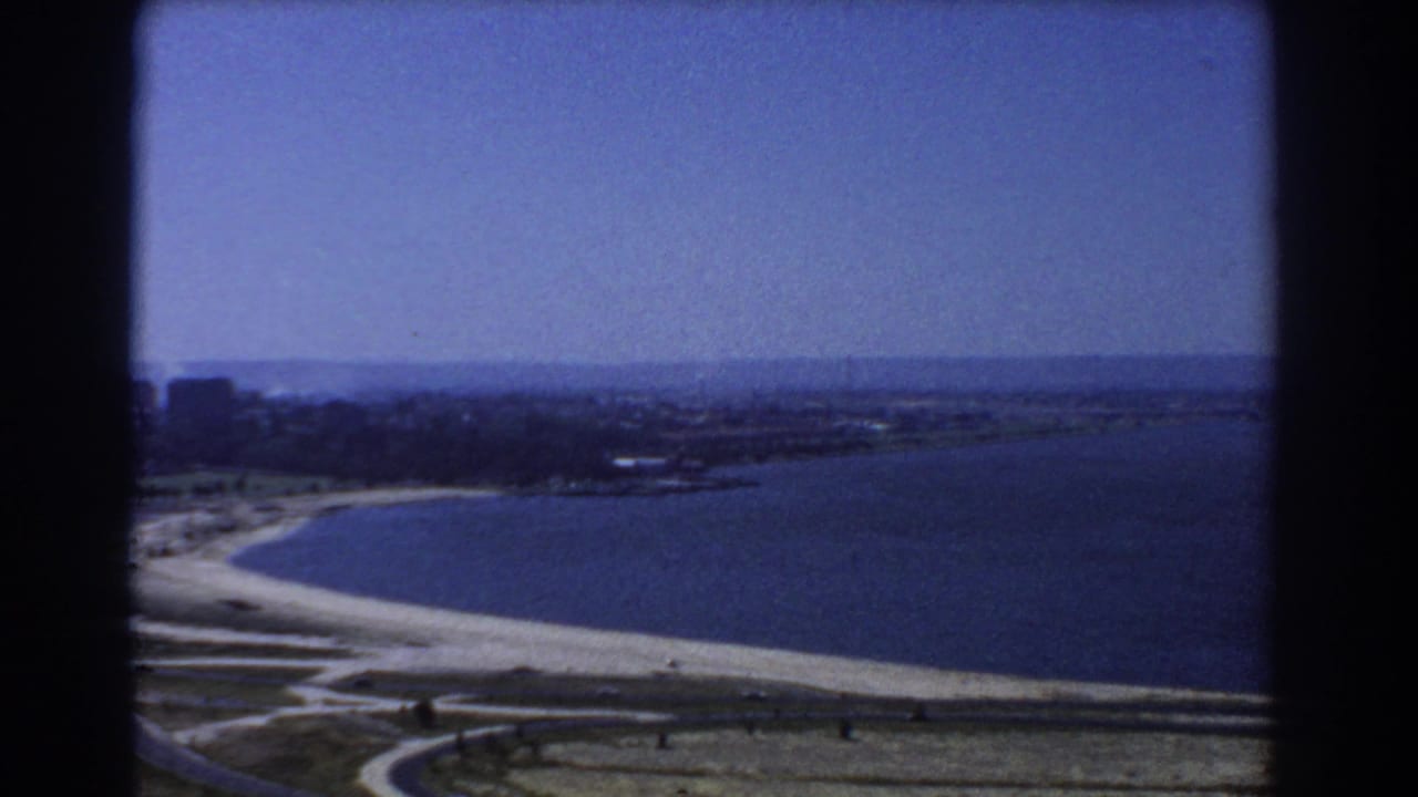 1967 Perth 8mm frame showing a high view over water, a pale shoreline, distant land, and dark film-frame edges.
