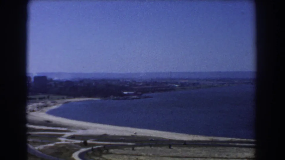 1967 Perth 8mm frame showing a high view over water, a pale shoreline, distant land, and dark film-frame edges.